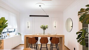 Een moderne keuken met een centraal eiland, barkrukken, hanglampen en een grote spiegel.