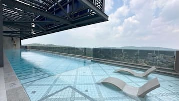 A rooftop swimming pool with clear blue water, a glass barrier, and a view of the cityscape.