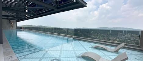 Una piscina en la azotea con agua azul cristalina, una barandilla de vidrio y vistas de la ciudad.