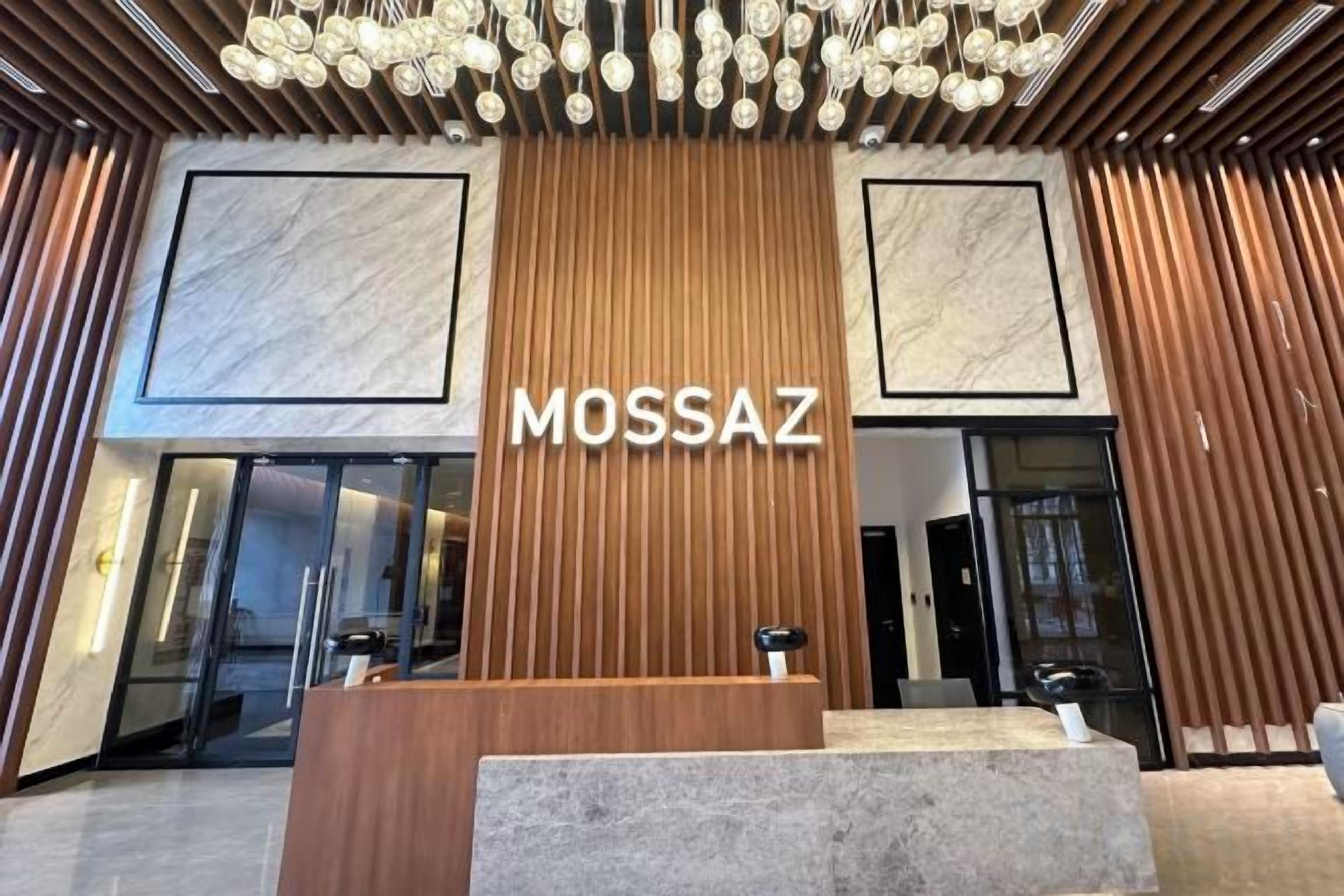 A reception area with a wooden panel wall, a marble-framed entrance, and a modern chandelier.