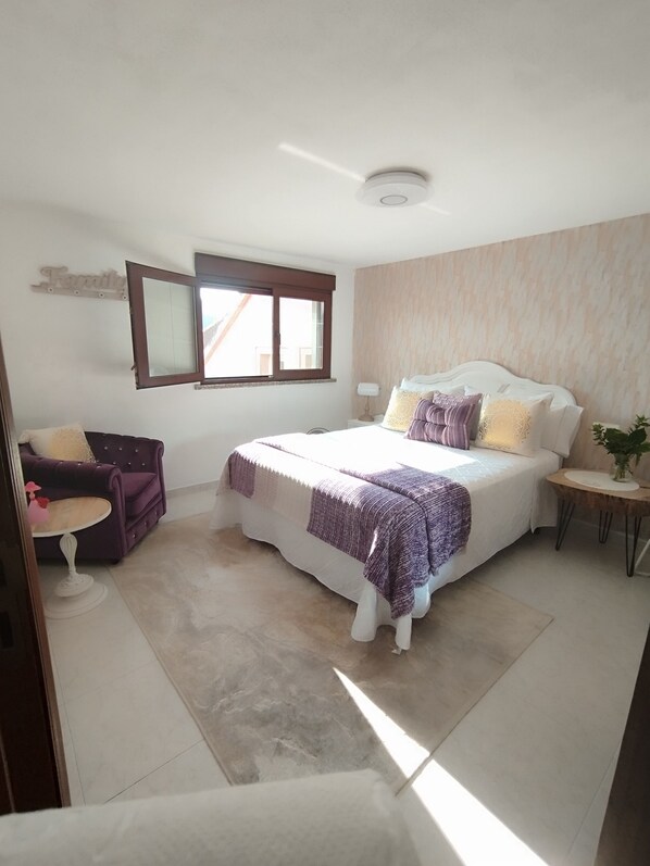 Une chambre à coucher avec un lit, une chaise, une petite table et une fenêtre.