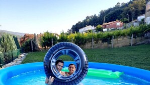 An inflatable pool with a tire in it, surrounded by a grassy area and houses in the background. - Casa SantaMaria (Lousame)