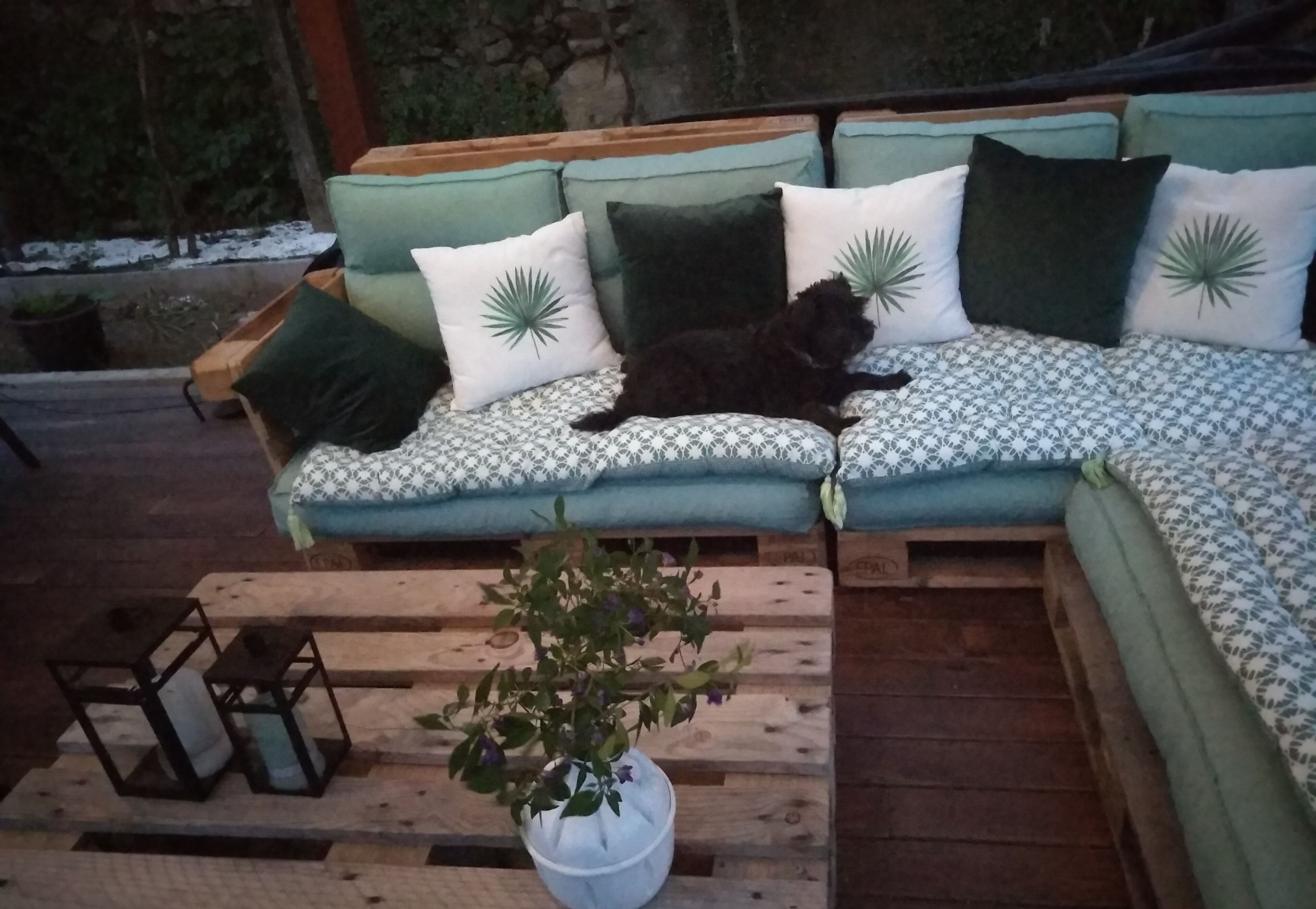 A wooden deck with a cushioned outdoor seating area, a potted plant, and a small table with candles.