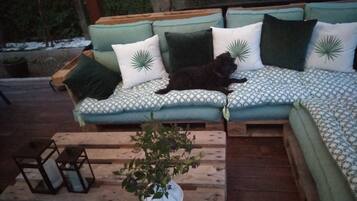 A wooden deck with a cushioned outdoor seating area, a potted plant, and a small table with candles.