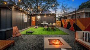 Een achtertuin met vuurkorf, buitenmeubilair, een barbecue en lichtjes.