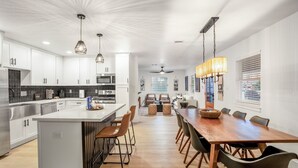 Een moderne keuken met witte kasten, een centraal eiland en een eethoek met een houten tafel en stoelen.