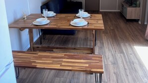 A modern living room with a wooden dining table set for four, a dark blue sofa, a TV on a wooden stand, and a door in the background. - CHALET WITH EXCEPTIONAL SEA VIEW (Saint-Raphaël)