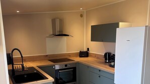 A compact kitchen with a built-in oven, a sink, a stove, a white refrigerator, and a microwave. - CHALET WITH EXCEPTIONAL SEA VIEW (Saint-Raphaël)