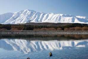 A mountain range reflected in a calm body of water with a clear sky. - Twin Stars (Lake Tekapo)