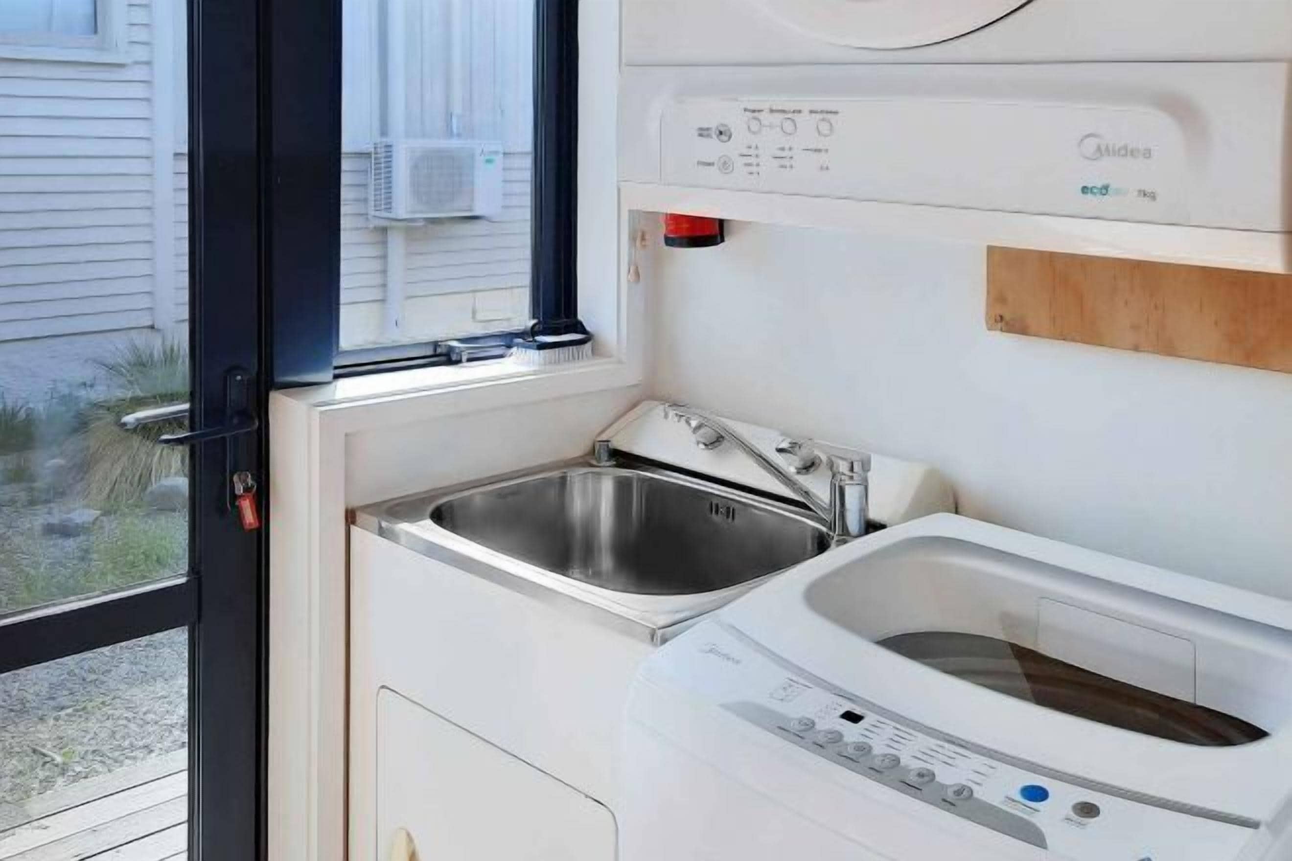 Una cocina compacta con un lavamanos de acero inoxidable, un horno empotrado y una ventana con unidad de aire acondicionado.