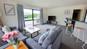 Ein modernes Wohnzimmer mit grauem Sofa, Couchtisch, Fernseher und Barbereich mit Hockern.