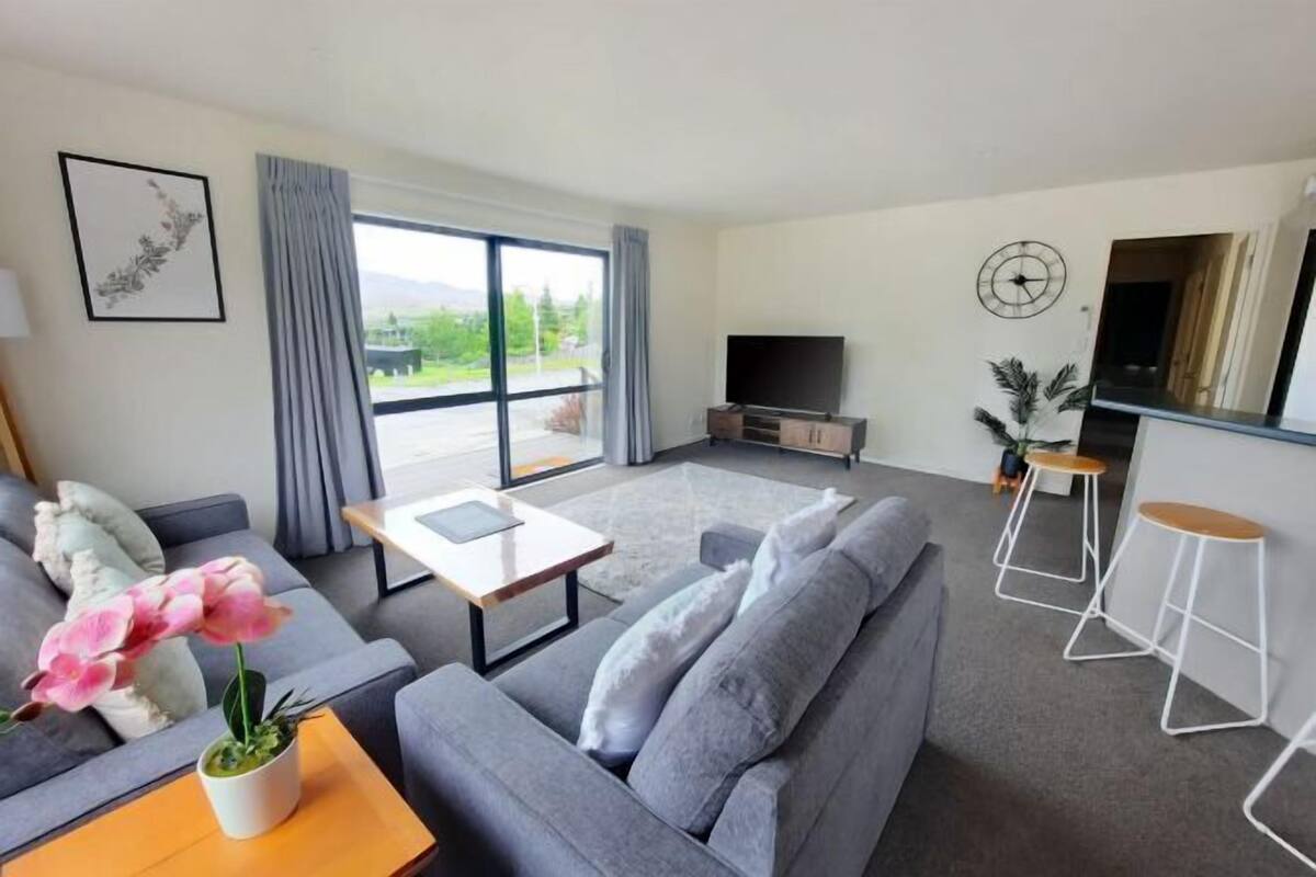 Ein modernes Wohnzimmer mit grauem Sofa, Couchtisch, Fernseher und Barbereich mit Hockern.