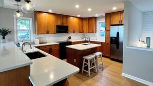 A modern kitchen with wooden cabinets, a stainless steel refrigerator, and a large island with stools.