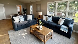 A living room with two dark blue sofas, a wooden coffee table, and a large window providing a view of the outdoors.