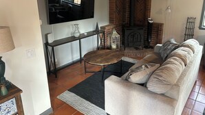 A living room with a sofa, a TV mounted on the wall, a fireplace, and a tiled floor. - Charming, quiet cottage in brilliant Fallbrook with AC, WiFi, private, Smart TV. (Fallbrook)