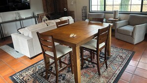 A cozy living room with a wooden dining table, comfortable seating, a fireplace, and a large window with a view of greenery. - Charming, quiet cottage in brilliant Fallbrook with AC, WiFi, private, Smart TV. (Fallbrook)