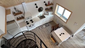 A modern kitchen with white cabinets, a stove, and a dining area with a table and chairs. - Chalet au toit vert (Sainte-Marguerite-du-Lac-Masson)