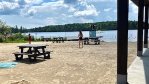 A beach with picnic tables and a lifeguard tower. - Chalet au toit vert (Sainte-Marguerite-du-Lac-Masson)