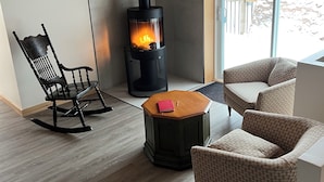 A cozy living room with a wood-burning stove, a rocking chair, and two patterned armchairs. - Chalet au toit vert (Sainte-Marguerite-du-Lac-Masson)