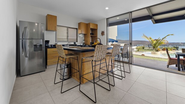 A modern kitchen with a stainless steel refrigerator, wooden cabinets, and a large island with bar stools. - Casa Familiar Alberca vista al lago 4 RC (Jojutla)