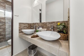 A modern bathroom with two large sinks, a mirror, and a potted plant.