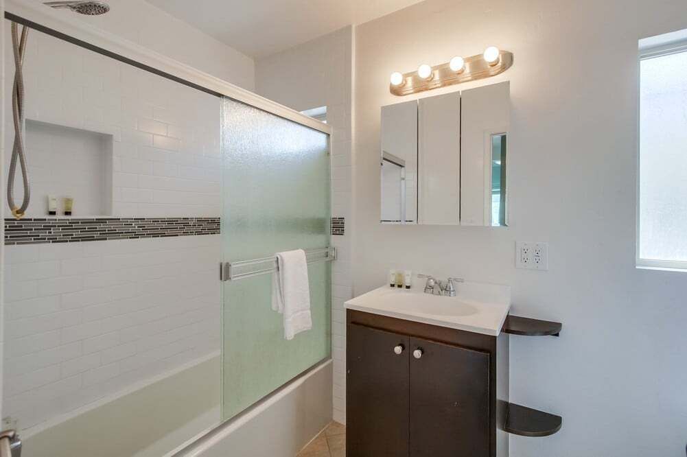 A bathroom with a glass-enclosed shower, a vanity with a mirror and lights, and a tiled backsplash.