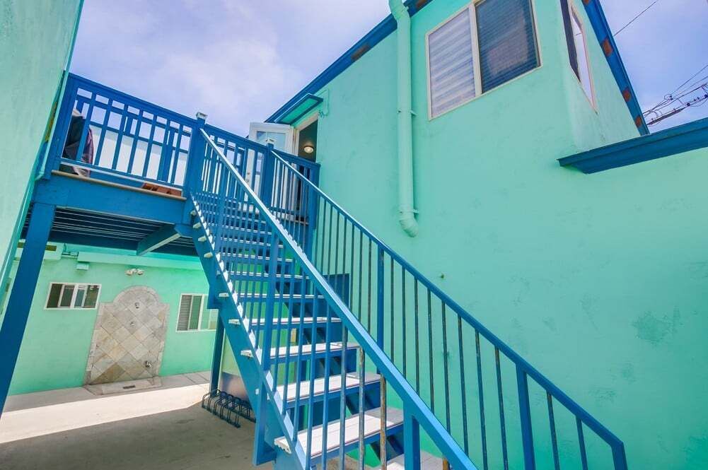 Una escalera conduce a una puerta con reja metálica, rodeada de muros azul verdoso y una barandilla azul.