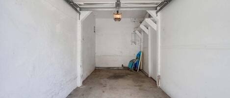 A garage with a concrete floor and white walls, featuring a single light fixture and a blue object leaning against the wall.