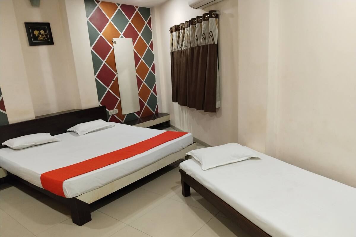 A hotel room with two beds, a colorful wall, a large window with curtains, and a framed picture on the wall.