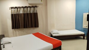 A hotel room with two single beds, a bathroom with a mirror, and an air conditioning unit on the wall. - Hotel Shree Muskan Palace (Ujjain)