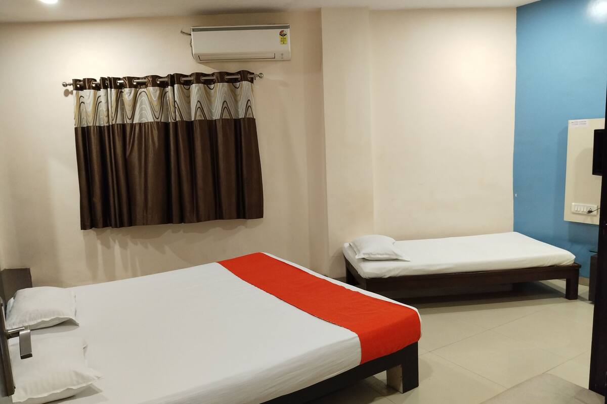 A hotel room with two single beds, a bathroom with a mirror, and an air conditioning unit on the wall.