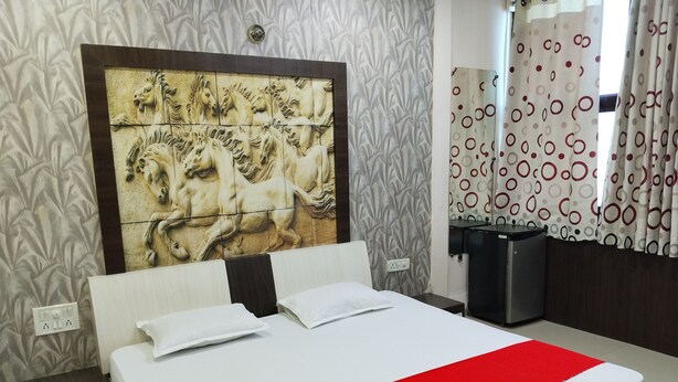 A hotel room with a large bed, a headboard with a horse mural, a small desk, and a mirror. - Hotel Shree Muskan Palace (Ujjain)