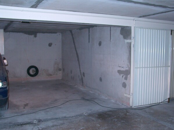 Un garage dans lequel une voiture est garée, avec un pneu posé sur le sol et un câble électrique qui traverse le sol.