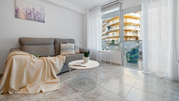 A modern living room with a grey sofa, a round coffee table, and a balcony with a view of an apartment building. - ALTAMIRA Apartment (La Pineda)