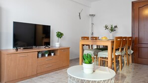 A modern living room with a flat-screen TV, wooden furniture, a dining table with chairs, and a small potted plant. - ALTAMIRA Apartment (La Pineda)