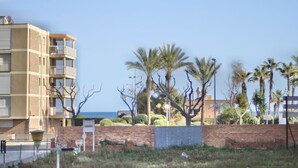 A multi-story building with balconies, a brick wall, and palm trees in the foreground. - ALTAMIRA Apartment (La Pineda)