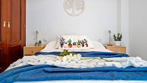 A neatly made bed with a blue blanket, a wall-mounted tree decoration, and a pillow with cacti. - ALTAMIRA Apartment (La Pineda)