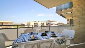 A balcony with a table set for two, featuring a striped tablecloth, white chairs, and a view of the cityscape. - MALDIVAS III Complex (La Pineda)