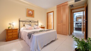 A bedroom with a bed, bedside tables, a nightstand, a wooden wardrobe, and a potted plant. - MALDIVAS III Complex (La Pineda)