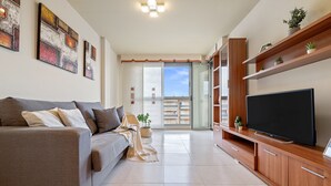 A modern living room with a sofa, TV, wooden entertainment unit, and artwork on the wall. - MALDIVAS III Complex (La Pineda)