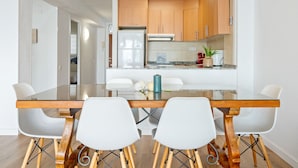 A modern kitchen with wooden cabinets, a refrigerator, and a dining area with a glass table and white chairs. - BELL RACÓ Superior (La Pineda)