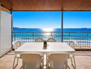 Un espace extérieur abrité où l’on peut prendre ses repas, avec vue sur la mer et un navire visible au loin.