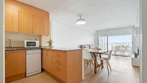 A modern kitchen with wooden cabinets, a dishwasher, and a microwave. There is a dining area with a table and chairs. - BELL RACÓ Superior (La Pineda)