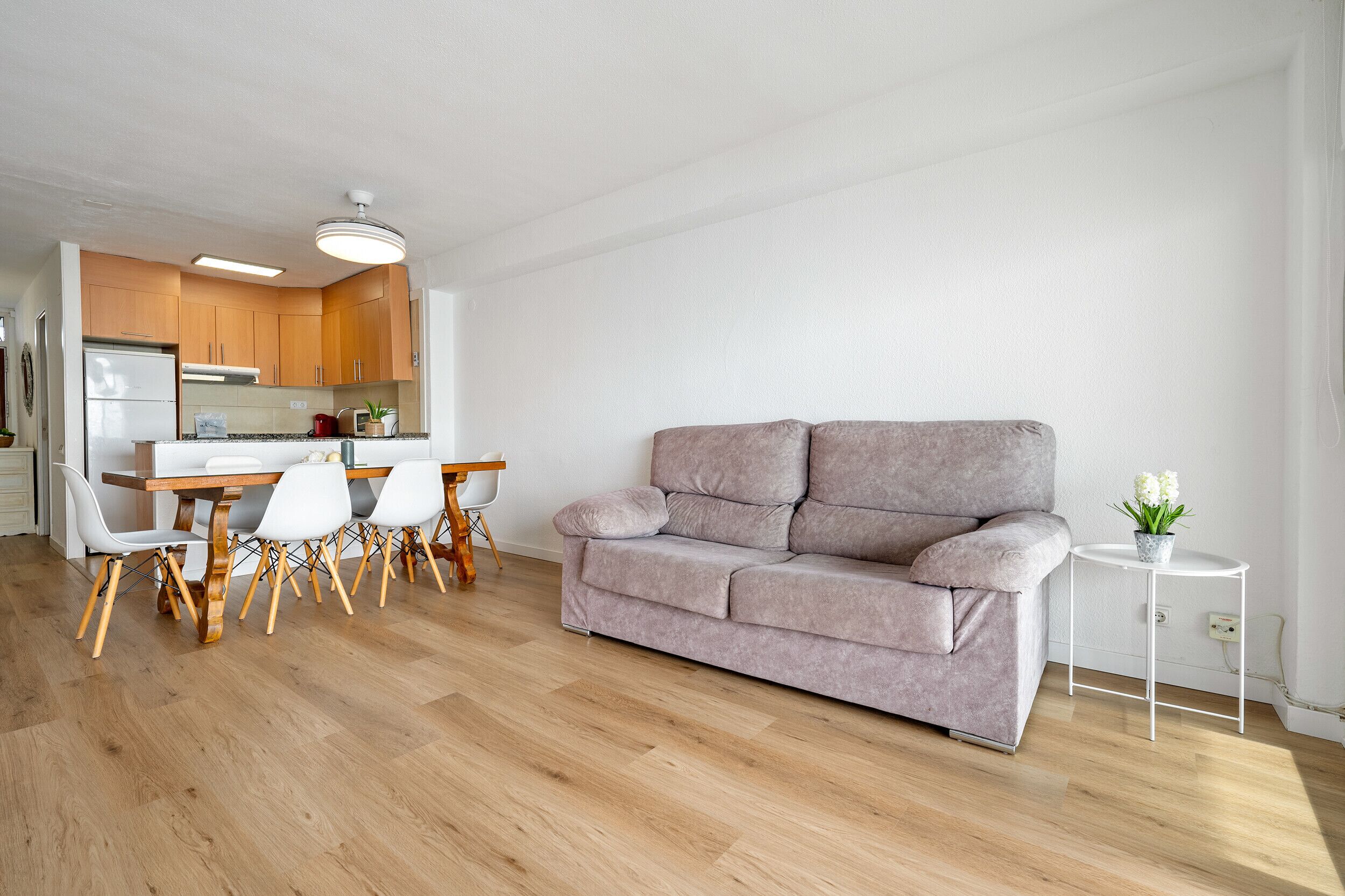 A modern living room with a grey sofa, a dining table with chairs, and a kitchen area in the background.