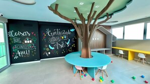 Uma sala de aula moderna com um grande mural de árvore, uma mesa redonda e bolas coloridas no chão.