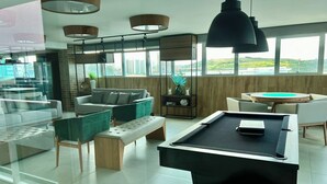 Uma sala de estar moderna com mesa de bilhar, assentos confortáveis e grandes janelas com vista para a cidade.