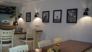 A dining area with a wooden table, white chairs, and a fruit bowl. There are framed pictures on the wall and a wine rack above the counter. - 2-bedroom house with Hot Tube, AC, WiFi. Enjoy a cozy stay near river. (Netretić)
