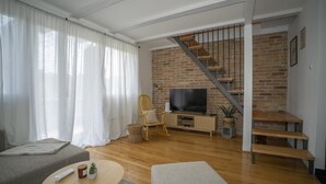A living room with a brick wall, a wooden staircase, a television, and a sofa. - 2-bedroom house with Hot Tube, AC, WiFi. Enjoy a cozy stay near river. (Netretić)