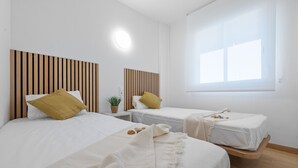 A hotel room with two beds, each with a wooden headboard, white bedding, and a small bedside table with a plant. - AQUAMARINA II Apartments (La Pineda)