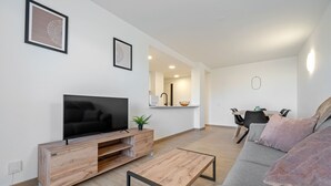 A modern living room with a flat-screen TV, wooden entertainment unit, grey sofa, and a coffee table. - AQUAMARINA II Apartments (La Pineda)